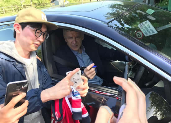 Arsenal boss Arsene Wenger looks in relaxed mood as he stops to sign autograph for fans outside club's training ground