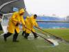 Stadium workers sweep rain water off the field toward a drain before match
